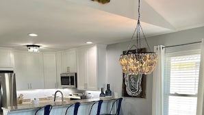 A modern kitchen with white cabinets, a central island with bar stools, a dining table with chairs, and a unique green fish head decoration. - Bayfront House w/ Hot Tub & Dock Access (Cape San Blas)