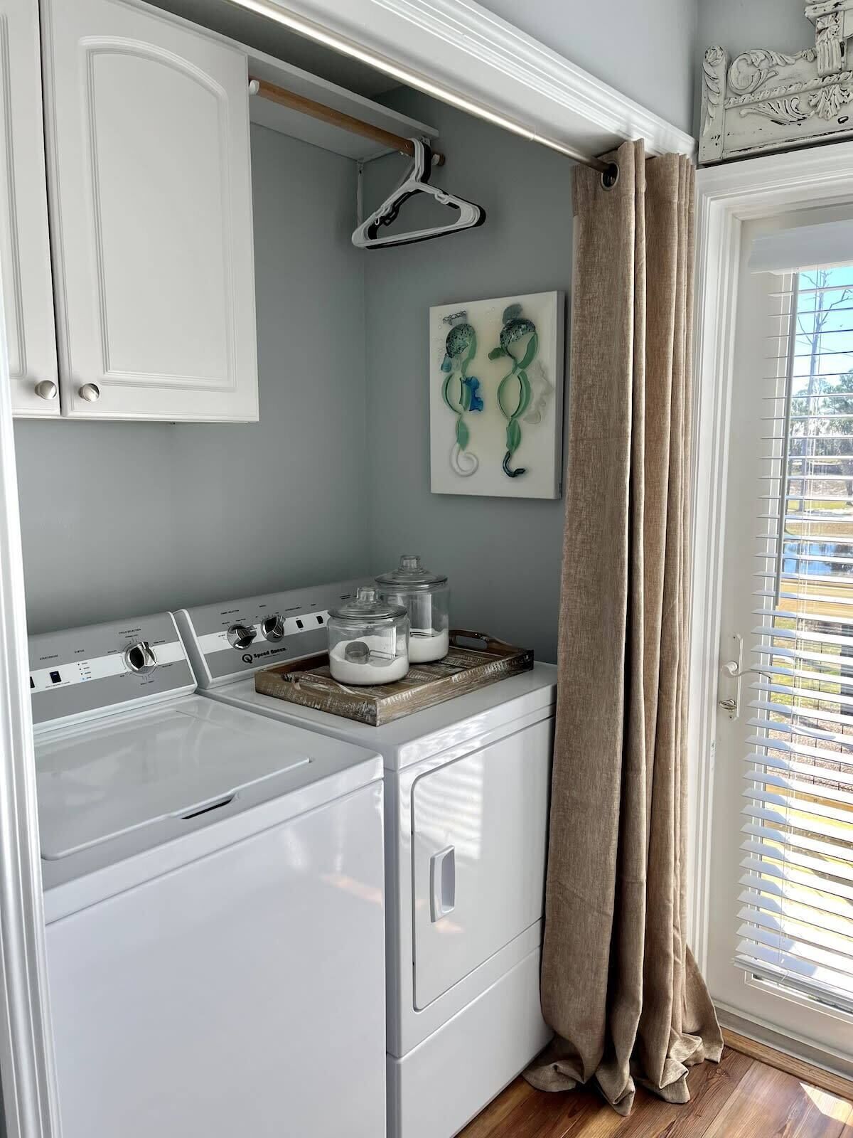 A laundry area with a washer and dryer, a drying rack, and a window with curtains.