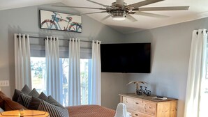 A hotel room with a bed, a ceiling fan, a TV, a wooden dresser, and a window with curtains. - Bayfront House w/ Hot Tub & Dock Access (Cape San Blas)