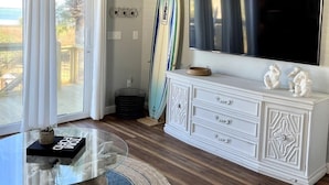 A living room with a ceiling fan, a surfboard, a TV, and a white cabinet. - Bayfront House w/ Hot Tub & Dock Access (Cape San Blas)