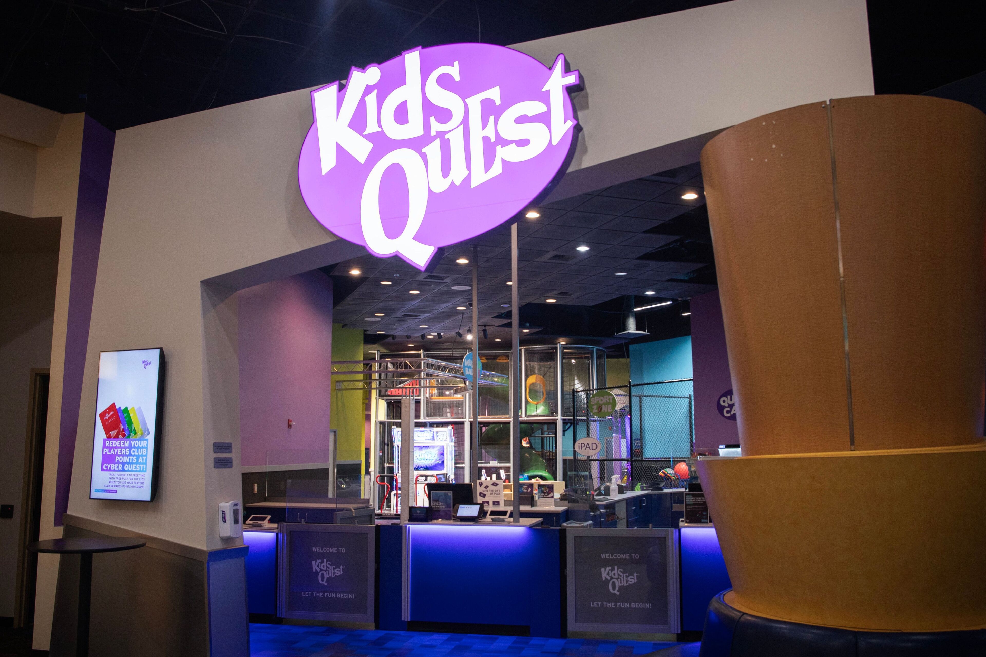The entrance to Kids Quest with a neon sign, a reception desk, and a large pillar.