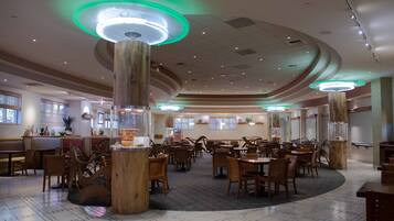 Un restaurant spacieux avec des tables et des chaises en bois, de grandes colonnes en bois et un éclairage d’ambiance vert.