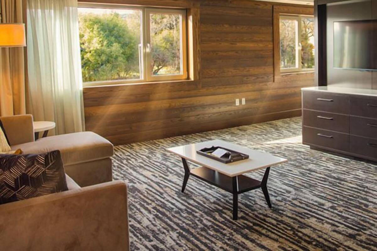 A modern hotel room with a large window, a sofa, a coffee table, and a TV.