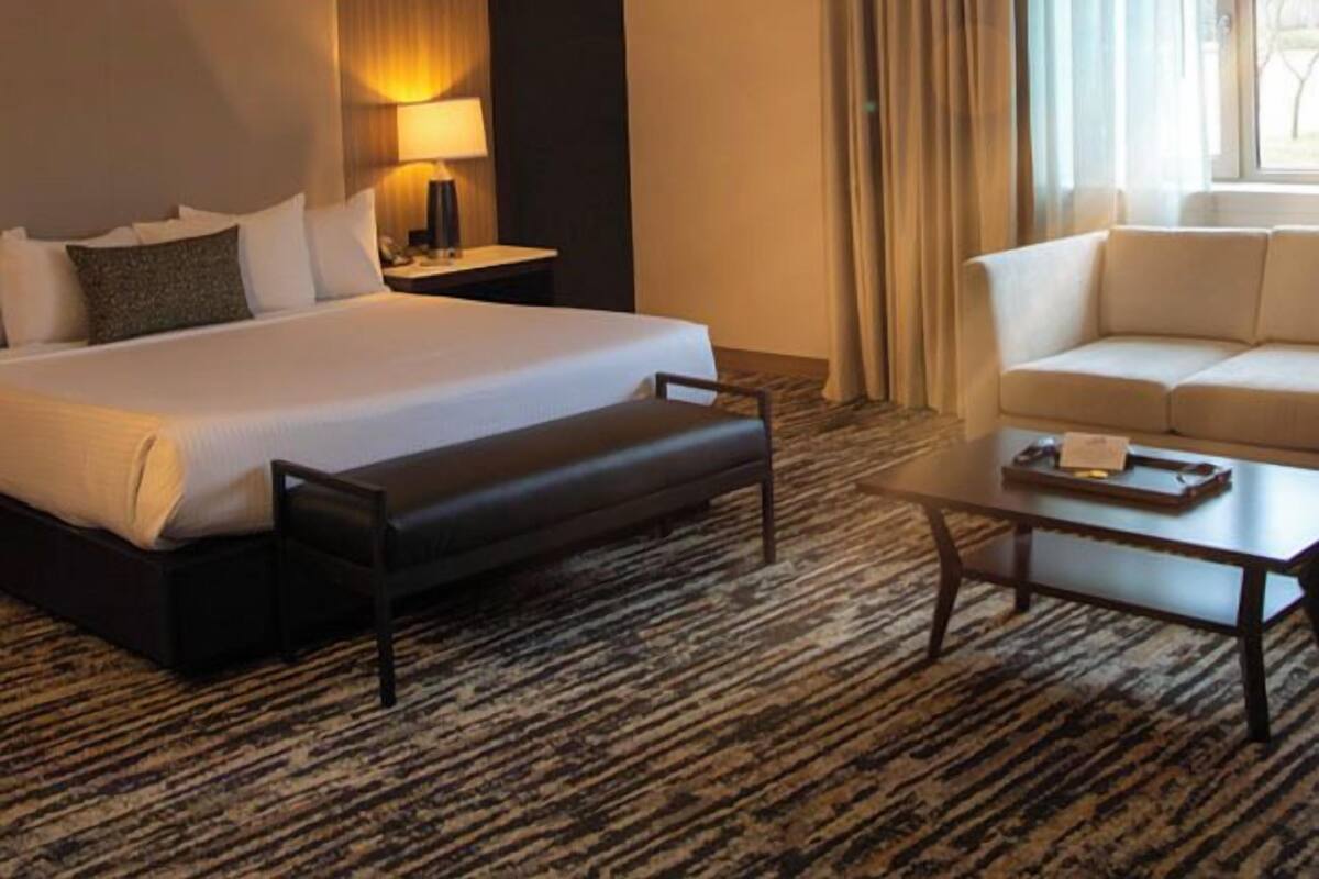 A hotel room with a large bed, a bedside table with a lamp, a sofa, and a coffee table.
