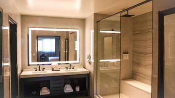 A modern bathroom with a large mirror, dual sinks, a glass-enclosed shower, and a built-in bench.