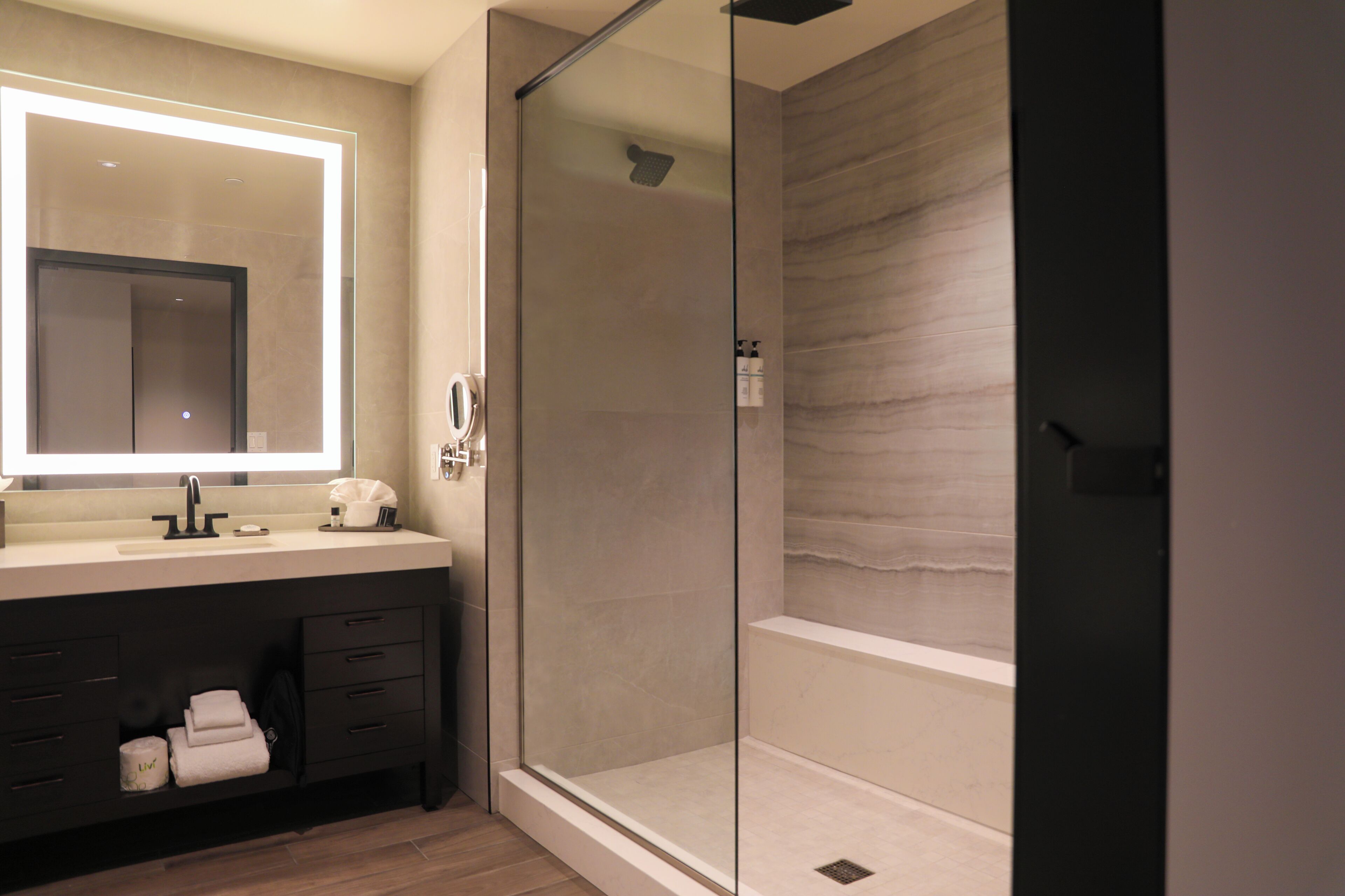 Un bagno moderno con doccia vetrata, uno specchio grande e un mobile lavabo scuro.