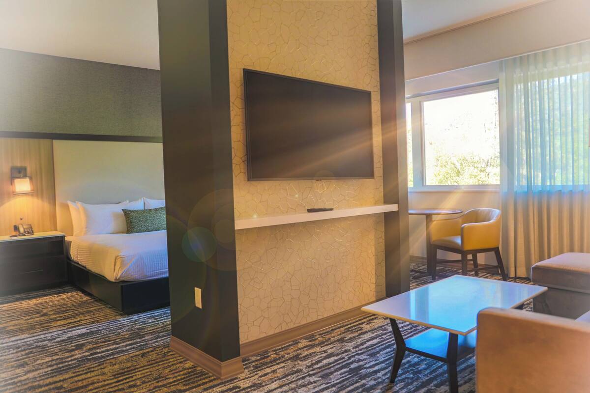 A hotel room with a bed, a TV mounted on the wall, a small table, and a chair.