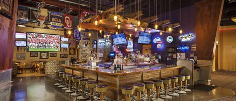A bar area with multiple screens, stools, and a counter.