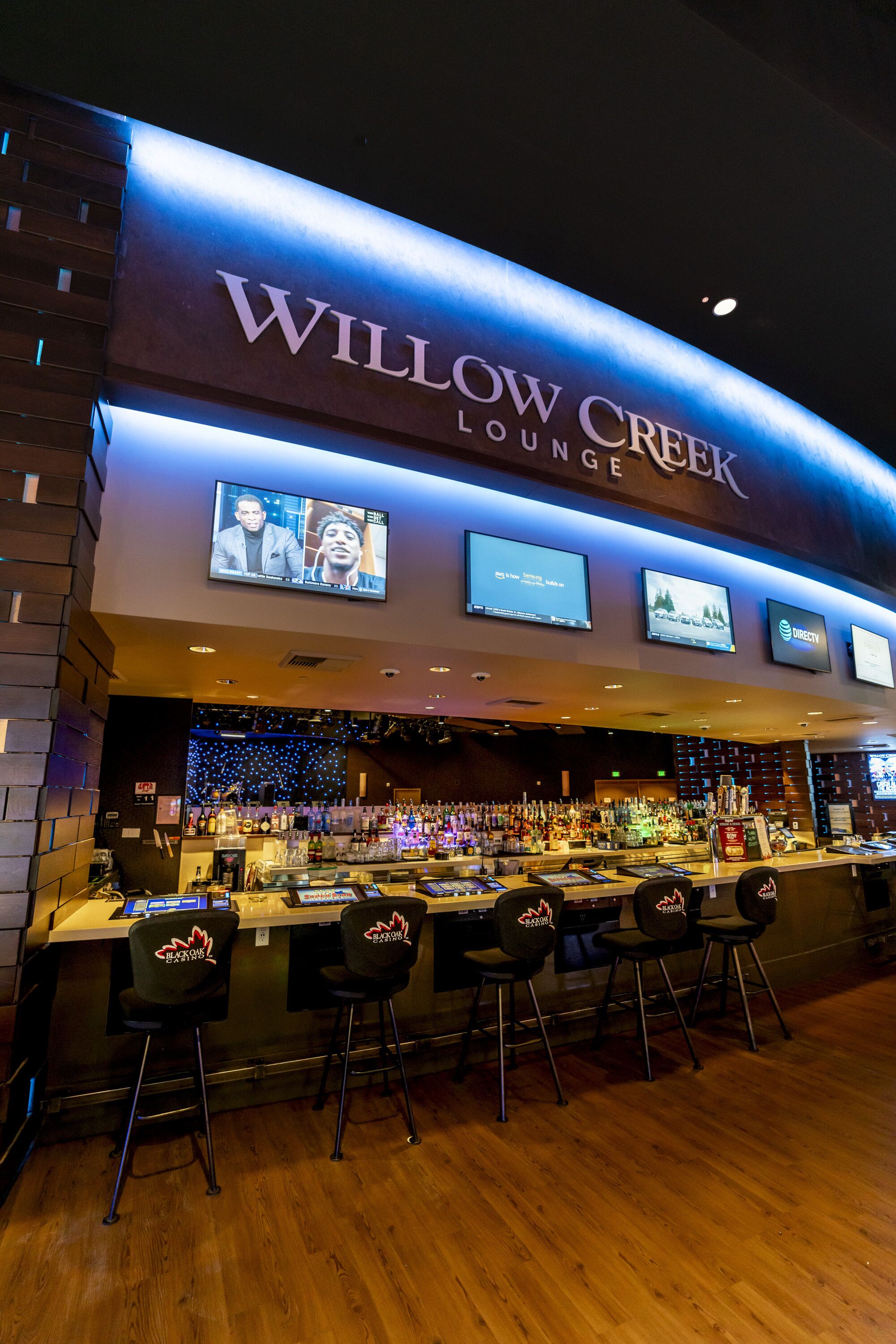 A bar area with a sign reading "Willow Creek Lounge" and multiple screens displaying content.