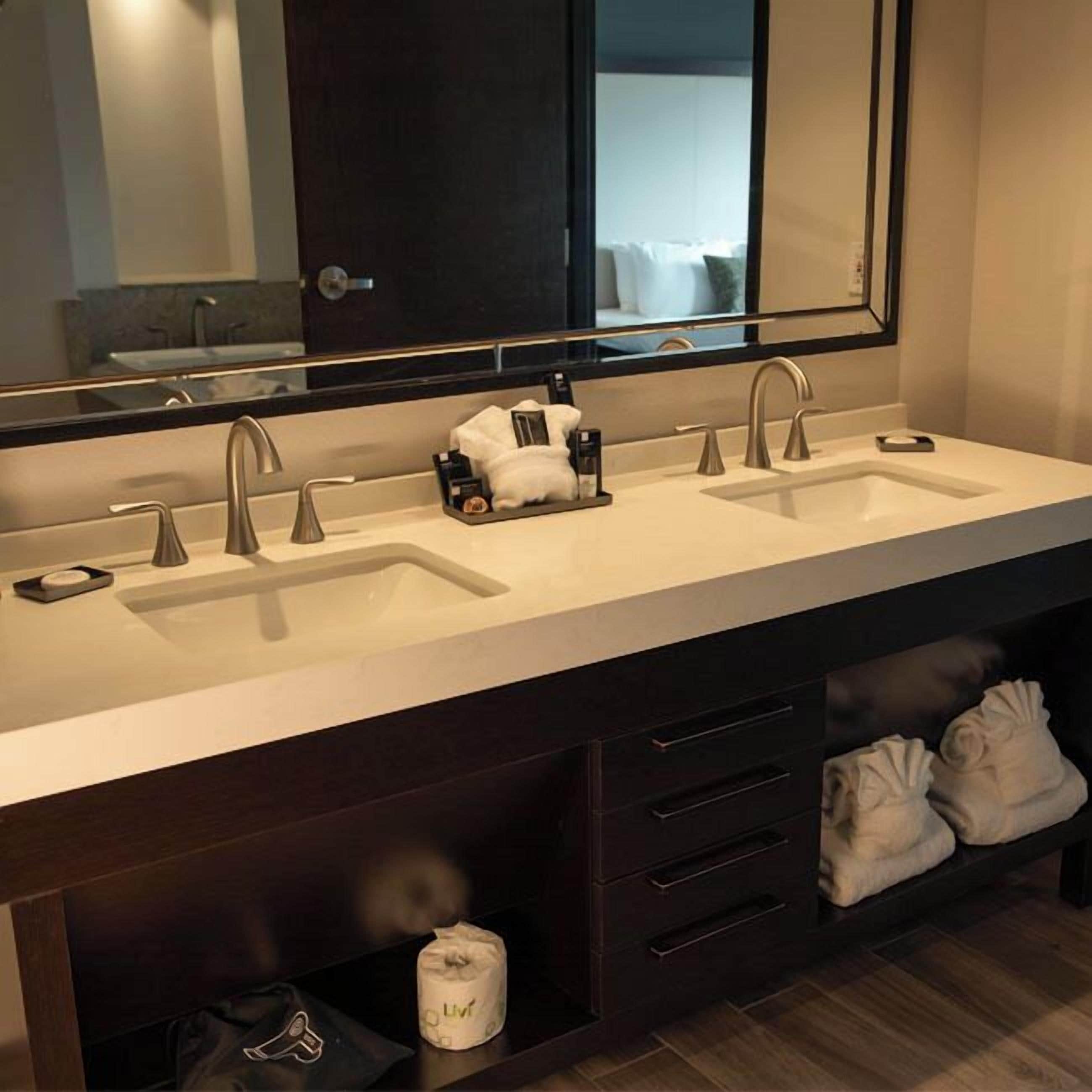 Un baño moderno con lavamanos doble, un espejo grande y un mueble con cajones y un perchero para toallas.