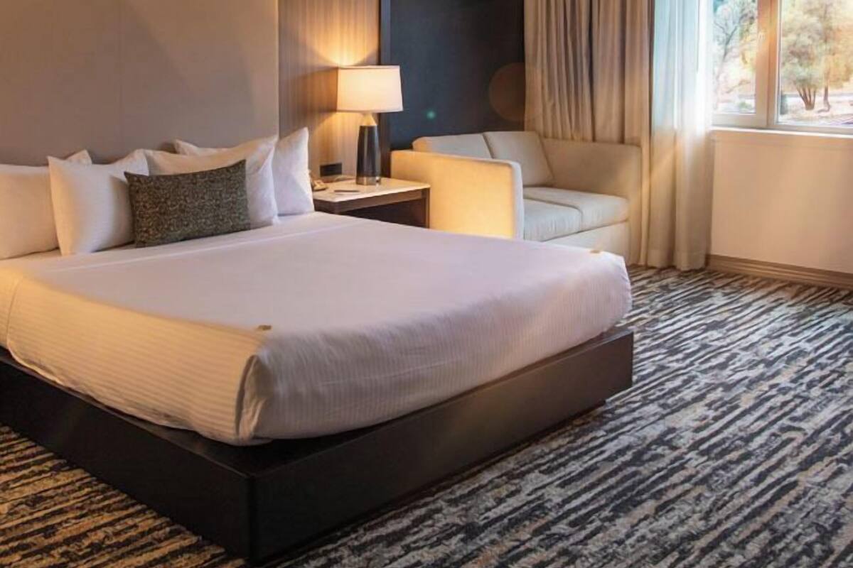 A hotel room with a large bed, a nightstand, a lamp, a chair, and a window with curtains.