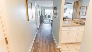 A narrow hallway with wooden flooring, white walls, and a kitchen area with white cabinets and a sink. - New,Direct Oceanfront at Amazing Bluewater Resort! (Myrtle Beach)