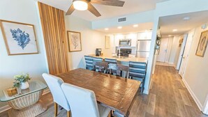A modern kitchen with a central island, wooden flooring, and a dining area with a glass-top table and white chairs. - New,Direct Oceanfront at Amazing Bluewater Resort! (Myrtle Beach)