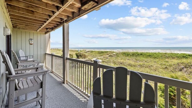 Een overdekt terras met Adirondack-stoelen, een houten balustrade en uitzicht op het strand.