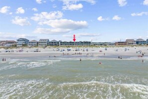 A beach with multiple buildings in the background, a clear sky, and waves in the foreground.