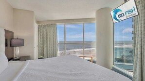 Habitación de hotel con una cama grande, televisión, lámpara y vista a la playa.