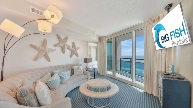 Una sala de estar moderna con un sofá, una mesa redonda de centro y decoración de estrella de mar en la pared. Un gran ventanal ofrece vistas al océano.