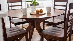 A round wooden table with four chairs, a potted plant, two muffins, and two white mugs.