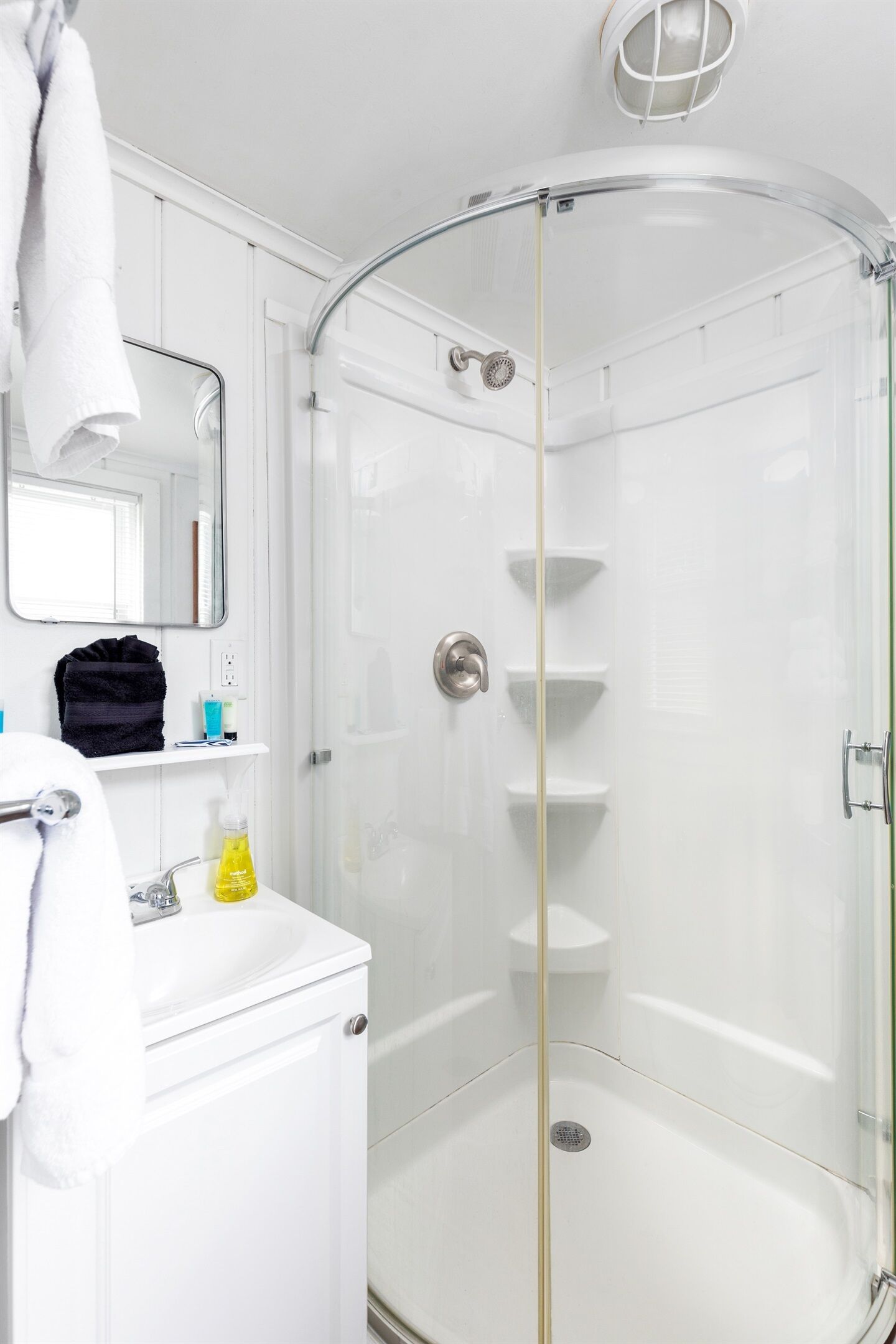 A modern bathroom with a glass-enclosed shower, white fixtures, and a mirror above the sink.