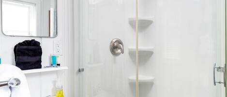 A modern bathroom with a glass-enclosed shower, white fixtures, and a mirror above the sink.