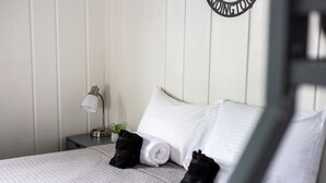 A neatly made bed with white linens, a small bedside table with a lamp, and a wall-mounted sign.