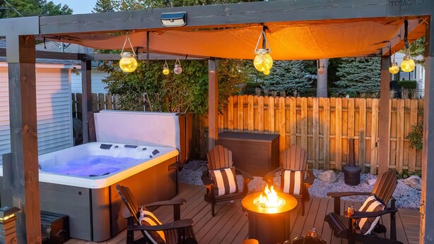 A wooden deck with a hot tub, outdoor seating, and a fire pit.