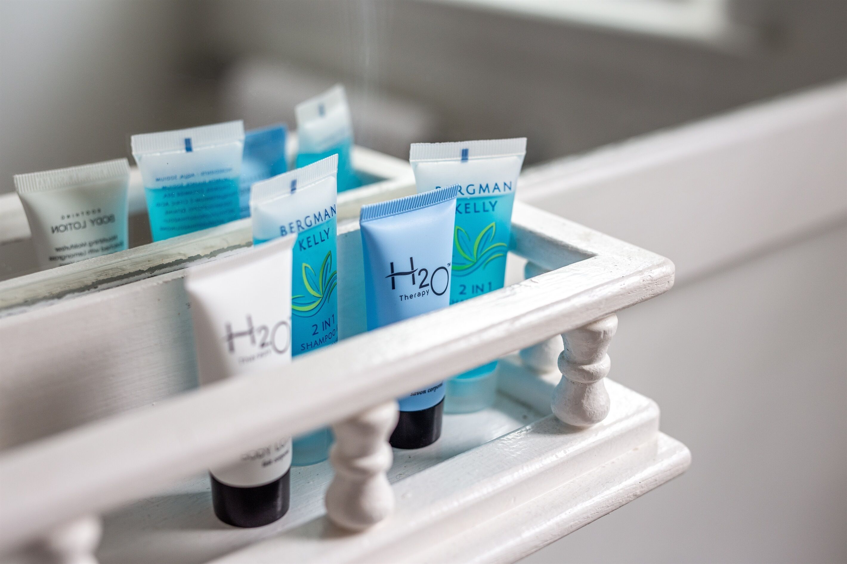 Una repisa de baño con varios artículos de aseo, incluyendo una botella etiquetada como “H2O Therapy” y varios tubos de productos Bergman Kelly.