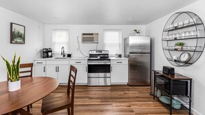 Una cocina moderna con armarios blancos, electrodomésticos de acero inoxidable, una mesa de comedor con sillas y una estantería con vajilla.