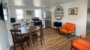 Une cuisine compacte dotée d’appareils électroménagers modernes, un coin repas avec des chaises en bois et un espace de vie lumineux comprenant un canapé et un fauteuil.