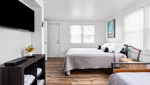 Une chambre à coucher avec un lit, un bureau avec une lampe, une télévision et une fenêtre avec des stores.