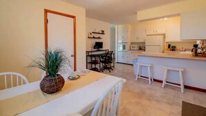 A compact kitchen with white cabinets, a dining area with a white table and chairs, and a small island with stools.