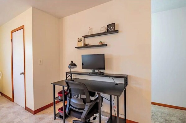 Een werkplek aan huis met een bureau, stoel, televisie en planken met decoratieve objecten.