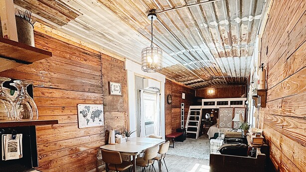 Un interno rustico con pareti in legno, una zona pranzo con sedie, una cucina con lavello e una scala che conduce a un garage.