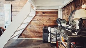 Una scala conduce a una camera da letto soppalcata con pavimento in legno, un letto, un comò e una lampada.