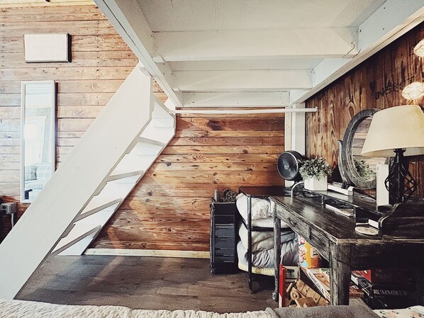A staircase leading to a loft bedroom with a wooden floor, a bed, a dresser, and a lamp.