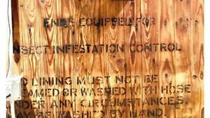 Una parete di legno con mensole esagonali che contengono asciugamani e una pianta, e un cartello riguardante il controllo dei parassiti.