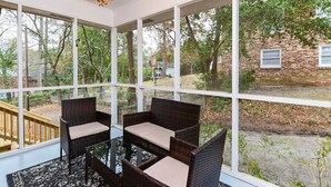 Un solárium con mobiliario de mimbre y grandes ventanales con vistas a un jardín trasero.