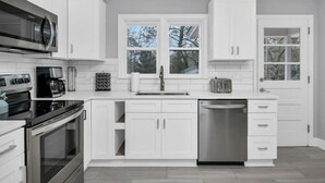 Cocina moderna con armarios blancos, electrodomésticos de acero inoxidable y una ventana que proporciona luz natural.