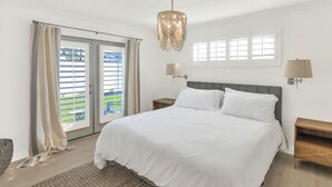 Ein Schlafzimmer mit einem großen Bett, zwei Nachttischen, einer Chandelüster und Blick aus dem Fenster.
