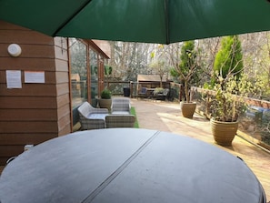A covered outdoor seating area with a table and two wicker chairs, surrounded by potted plants and a wooden deck.