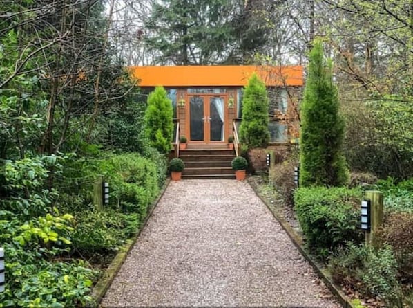 A pathway leading to a building with a wooden door and a sign above it.