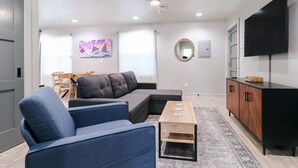 Una sala de estar moderna con un sofá seccional, una mesa de centro, un televisor y un ventilador de techo.