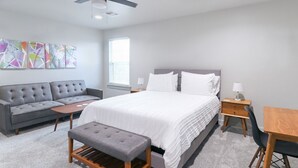 Un dormitorio moderno con una cama grande, un sofá gris, un escritorio de madera y una mesita.