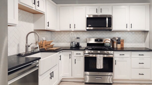 Cocina moderna con gabinetes blancos, electrodomésticos de acero inoxidable y encimera negra.