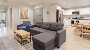 Una sala moderna con un sofá seccional, una mesita y un comedor con mesa y sillas de madera.