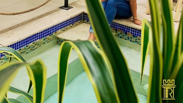 Eine Person sitzt am Pool, vor einem Seilzaun, mit einem Holzstuhl und einem Blumentopf im Hintergrund.