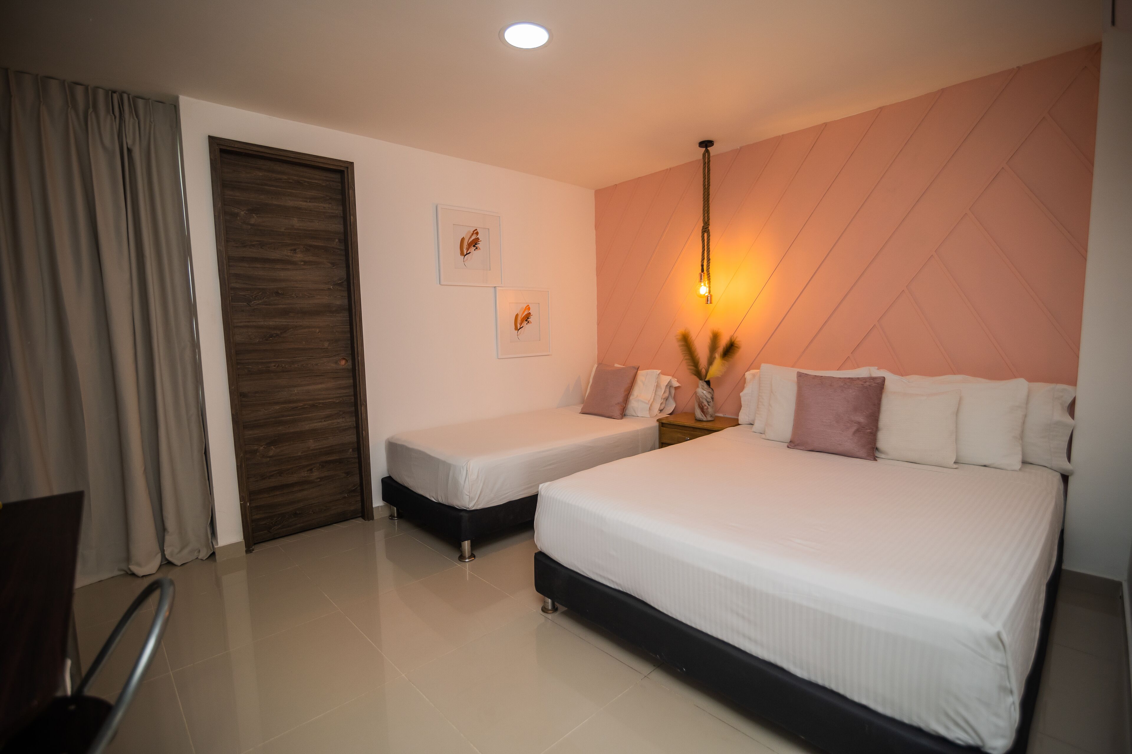 A hotel room with a large bed, a smaller bed, a wooden door, and a wall-mounted light fixture.