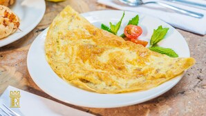 Ein Frühstücksteller mit einer Omelette, einem Croissant und einem Glas Orangensaft auf einer Marmortischplatte.