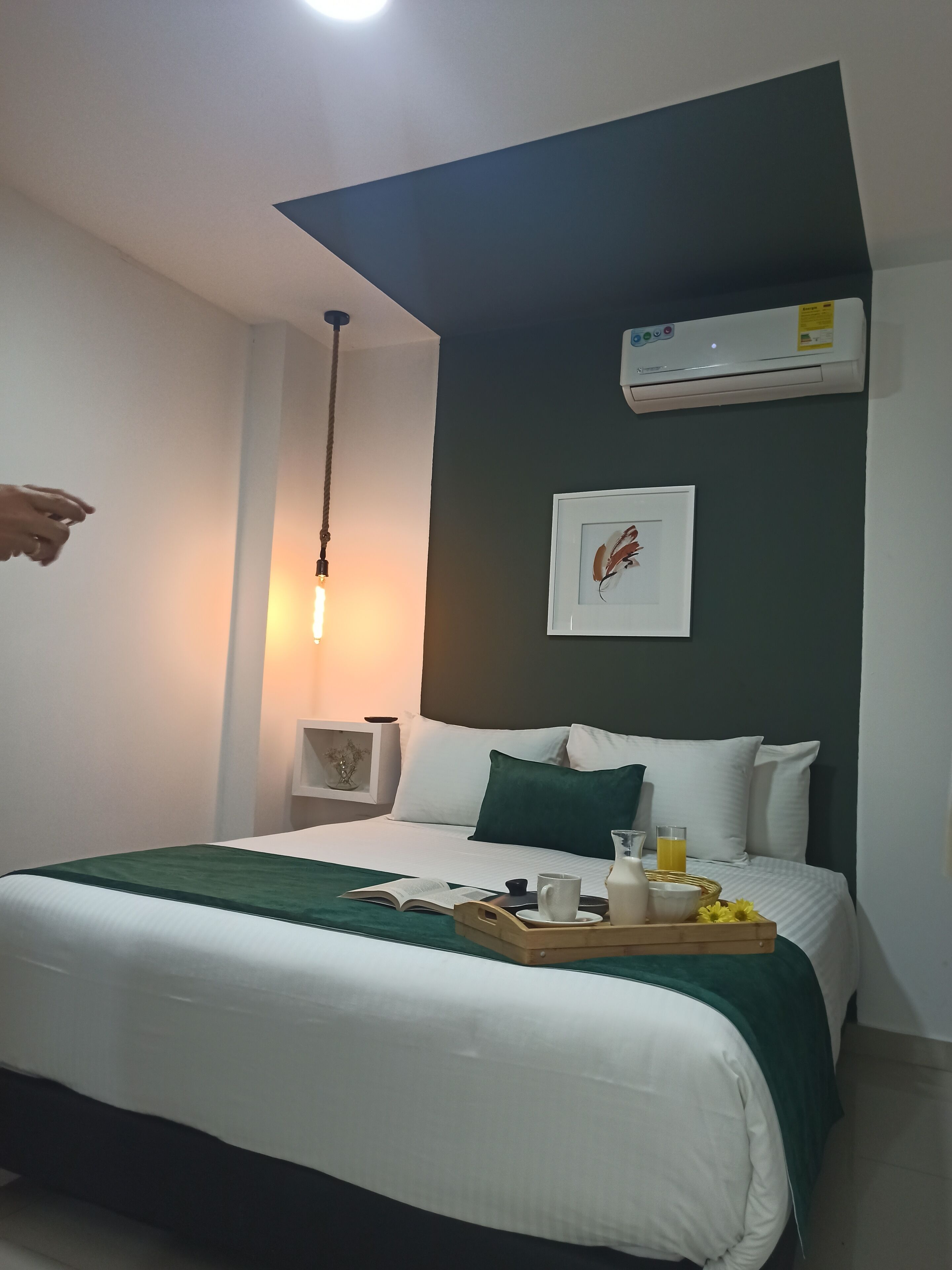 Ein Hotelzimmer mit Bett, Nachttisch, Wandklimaanlage und einem gerahmten Bild an der Wand.