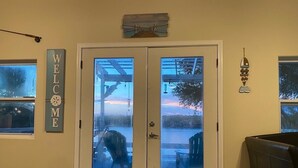 A room with a double door, a 'WELCOME' sign, a small table, and a chair.